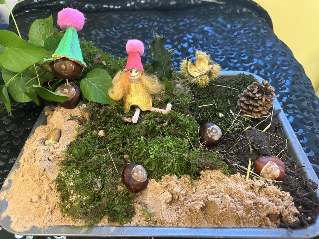 A fairy garden made from moss, sand, conkers and pine cones with small handmade fairies