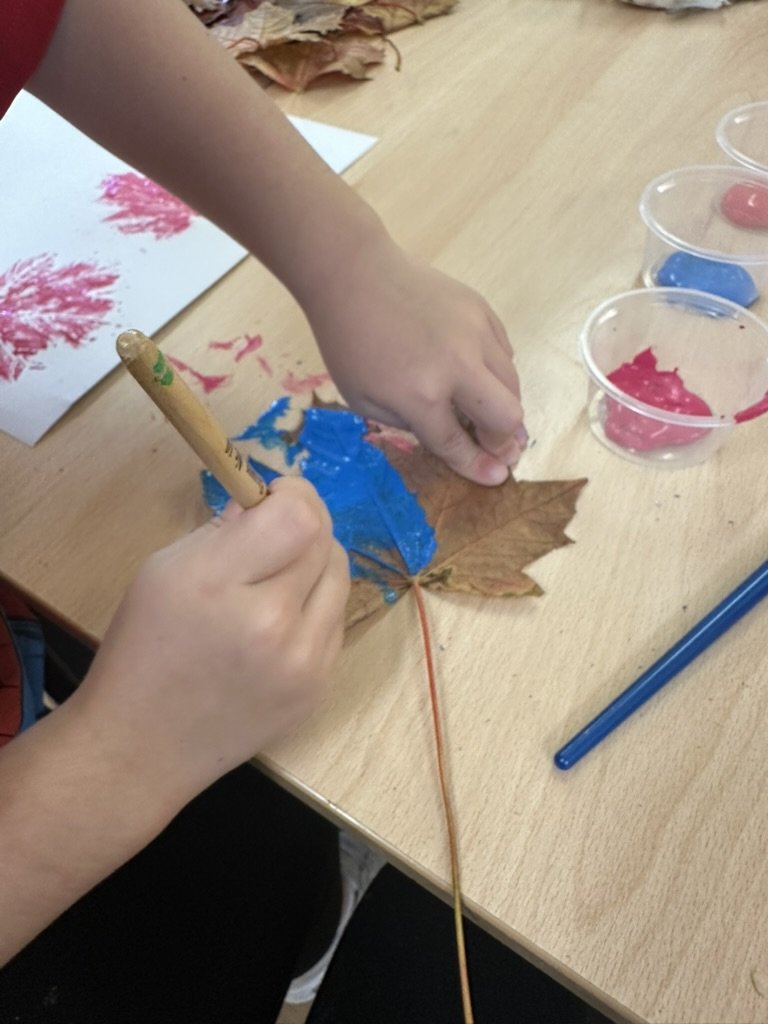 Child painting a maple leaf blue to make leaf prints