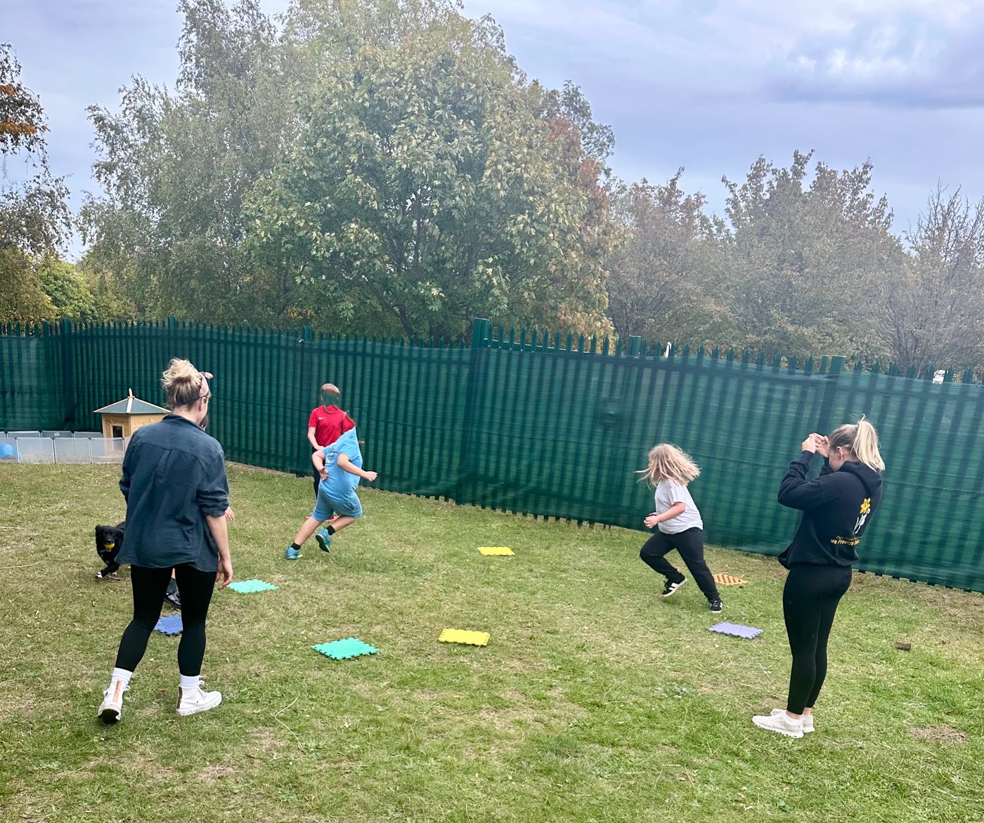 Children and staff playing a running game on the grass with coloured sensory mats