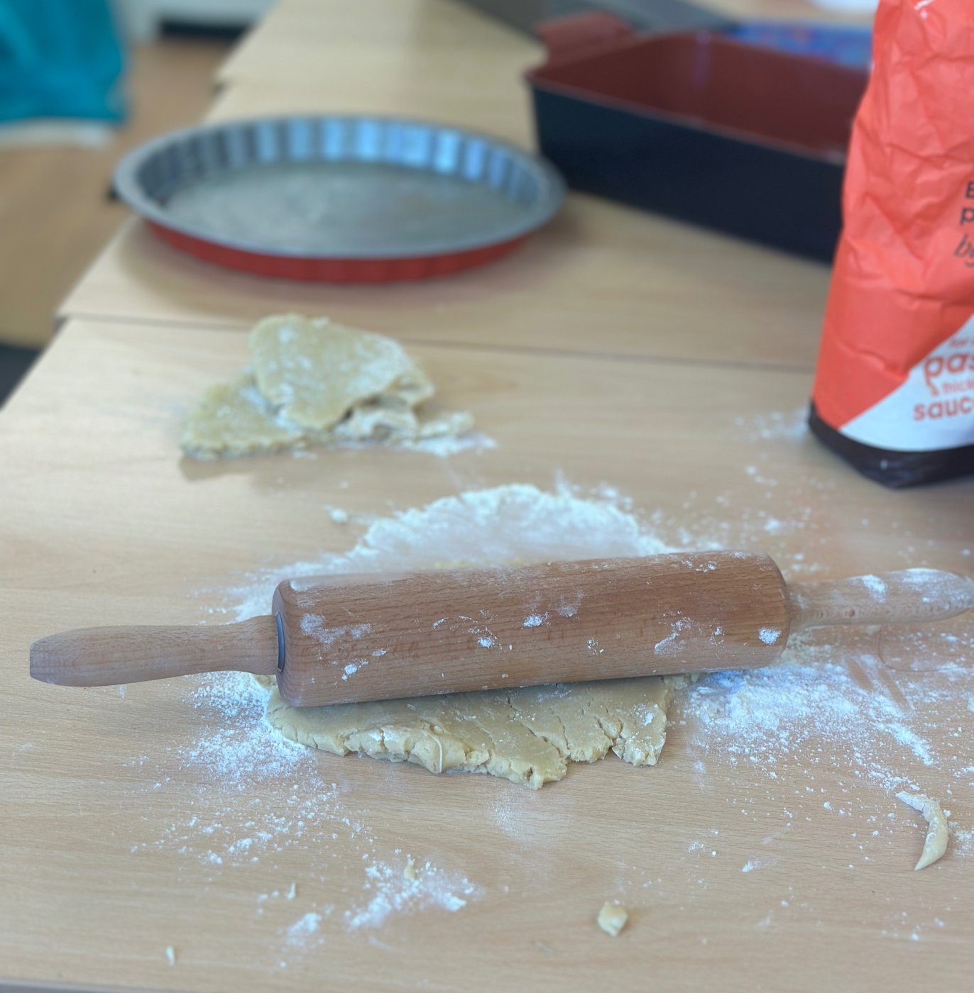 Pastry dough being rolled out with a wooden rolling pin on a floured table